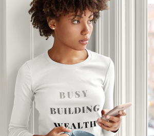 Woman wearing white long sleeve shirt that says "Busy Building Wealth"