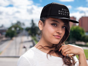 Woman wearing black trucker hat that says "Busy Building Wealth"