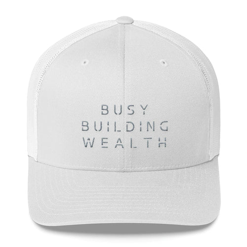 White trucker cap that says Busy Building Wealth in gray